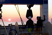 Crewmen watching sunset over the North Sea, from a fishing trawler. September 2008.