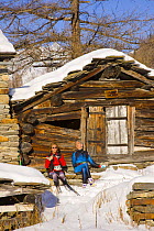 Cross country skiers resting outside wooden cabin in Gran Paradiso NP, Valnontey, Aosta valley, Italian alps.