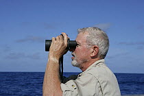 Man looking out to sea with binoculars, aboard Amel 54 ketch "Hollis" on delivery from Martinique, Caribbean. 2006.  Model and property released.