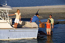 Man passing a picnic basket from the stern of Surf Hunter 33 to a couple in the shallows, Marco Island, Florida, USA. Model and property released, 2007.