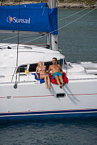 Couple sitting on the gunwale onboard a Sunsail yacht cruising in the British Virgin Islands, Caribbean. Model released, March 2006.