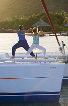 Couple doing yoga on bow of Sunsail Lagoon 410 catamaran, British Virgin Islands, April 2006. Model Released.