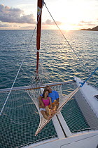 Couple relaxing in hammock on the stern of a Sunsail Lagoon 410 catamaran at sunset. British Virgin Islands, April 2006. Model released and property released.