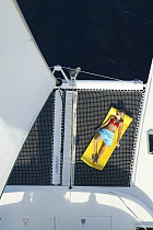 Girl in bikini sunbathing on board Lagoon 470 Sunsail charter catamaran ^KooLau^, anchored off the British Virgin Islands, January 2004. Model released.