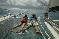 Couple relaxing on trampoline of Lagoon 470 Sunsail charter catamaran "KooLau", British Virgin Islands, January 2004. Model and property released.