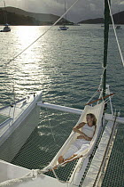 Woman relaxing in a hammock over trampoline of Lagoon 470 Sunsail charter catamaran "KooLau", British Virgin Islands, January 2004. Model and property released.