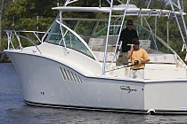 Man on mobile phone, fishing from the stern of a sportsfisher.  Model and property released.