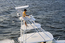 Man steering a sportfisher boat from the tuna tower.  Model and property released.