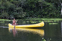 Young Wounaan Indian man paddles his canoe down the Charges River, Panama, November 2008