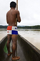 Young Embera Indian man heading down the Chagres River, dressed in the traditional beaded skirt (of the Panama flag) Panama, November 2008