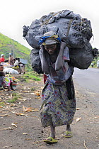 Woman carrying heavy load of charcoal bags to the market, on the road from Sake to Goma, North Kivu, Democratic Republic of Congo, Africa, March 2009