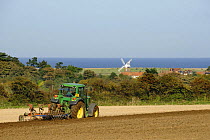 Tractor with combined plough and disc harrow on coastal farmland with Cley windmill in distance, Weybourne, Norfolk, UK, October,