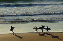 Surfers walking along Sandymouth beach, Cornwall, UK