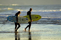 Two surfers walking along the beach, Sandymouth bay, Cornwall, UK.