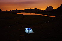 Mountaineers in tent at dusk, Anayet alpine lake shore with Midi d'Ossau peak in the background, Pyrenees mountains, Huesca, Aragon, Spain