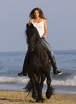 Purebred Friesian stallion ridden by woman on  Summerland Beach, Ojai, California, USA Model released