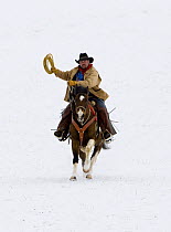Cowboy riding in snow, ready to throw a loop, Flitner Ranch, Shell, Wyoming, USA Model released