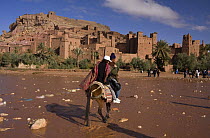 Tourists crossing shallow river on horseback, Aït Benhaddou Kasbah UNESCO site, Morocco. November 2008.