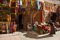 Woman looking at goods outside a carpet shop in Essaouira town, Morocco, November 2008. Model Released. (This image may be licensed either as rights managed or royalty free.)