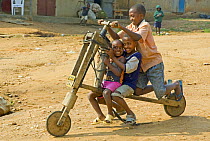Three children on a wooden scooter, Uganda, January 2009