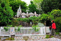 Woman standing beside little chapel in Guernsey, Channel Islands, May 2009. A French priest built it at the beginning of the 20th century with seashells, pebbles and colourful pieces of broken ceramic...