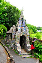 Woman standing beside little chapel in Guernsey, Channel Islands, May 2009. A French priest built it at the beginning of the 20th century with seashells, pebbles and colourful pieces of broken ceramic...