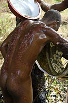 Washing the wounds of young man who has recently been through the initiation ceremony in which his flesh is wounded to create scars that represent being swallowed by a crocodile and re-born as a croco...