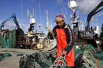 Crew mending nets on quay beside fishing trawlers. Cullivoe, Unst, Shetland, April 2008.