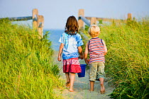 A young brother and sister walking towards the beach at Center Hill Preserve beach, Plymouth, Massachusetts, USA. Model Released. May 2008