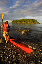 Kayaker about to enter the water, Porcupine Islands, Acadia National Park, Maine, USA. Model Released. June 2008