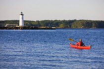 Woman kayaking on sea, New Castle, New Hampshire, USA. Portsmouth Harbor Light is in the distance. Model Released.   May 2008
