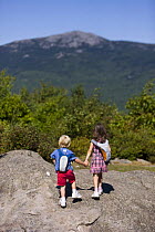 A young brother and sister holding hands while hiking on Gap Mountain, Troy, New Hampshire, USA. Mount Monadnock is in the distance. Model Released. August 2008