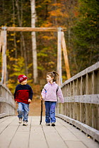 Two children (ages 4 and 6) walking across a wooden suspension bridge, Lincoln's Woods Trail, White Mountains National Forest, New Hampshire, USA. Model Released. October 2007