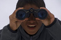 A young Inupiaq whaler looking for whales through binoculars during spring whaling season, off the Arctic coastal village of Point Hope, Chukchi Sea, Alaska, May 2008