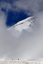Skiers under Mount Elbrus, Europes highest mountain (5,642m) surronded by clouds, Caucasus, Russia, June 2008