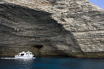 Limestone coastline, with one of the boats that cross to and from the Lavezzi Islands (approximately 10km SE) exiting a cave, Bonifacio, Corsica, France, September 2008