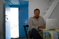 Photographer, Stefano Unterthiner, using laptop computer, Antikythera island, Greece, September 2008