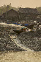 A man launches his shrimp fry fishing boat down the mud bank at low tide into the Sibsa River, Nolian Village, Sundarbans, Khulna Province, Bangladesh, March 2006