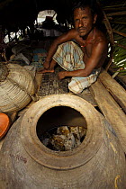 Boatman on the honey collectors boat beside the large clay jar where harvested honey and honeycomb are stored, Sundarbans, Khulna Province, Bangladesh, April 2006