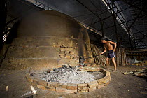 Worker tending the fire of a charcoal kiln. Charcoal production near Taiping, Malaysia, where (Rhizophora apiculata) mangrove wood from the Matang Mangroves is used to produce charcoal using tradition...
