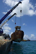 Cranes lowering the hulk of tugboat ''Blue Plunder'' into the water prior to towing out to sea and sinking. Nassau, Bahamas. August 2007.