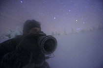 Photographer, Sven Zacek, in snow covered landscape at night, Riisitunturi National Park, Finland, February 2009