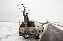 Researcher holding tracking antennae standing on the back of truck, collecting data on bison, Bialowieza NP, Poland, February 2009