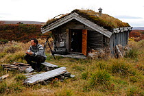 Photographer, Vincent Munier, sitting outside small traditional grass roof hut, Forollhogna National Park, Norway, on location for Wild Wonders of Europe, September 2008
