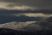 Hills in the Forollhogna National Park covered in a thin layer of snow against a dark storm sky, Norway, September 2008