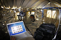 Reviewing photos on a laptop inside hide with binoculars and camera, La Serena, Extremadura, Spain, April 2009
