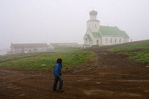 Person walking along road in mist with Russian orthodox church (1936) behind, St George, Saint George Island, Pribilof Islands, Alaska, USA
