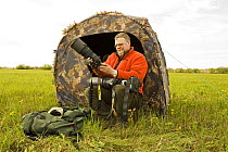 Photographer, Lassi Rautiainen, sitting outside tent, being used as a hide, with camera, Estonia, May 2009