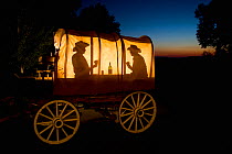Silhouette of two cowboys playing cards and drinking in a wagon, Wyoming, USA, September 2006, Model released