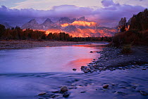 First light on mountains of the Teton range with storm clouds above and Snake river in the foreground, Grand Teton National Park, Wyoming, USA